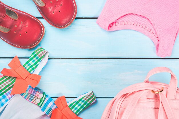 Accessoires de petite fille. Sac rose avec une robe colorée, des chaussures et une chemise sur une surface en bois pastel bleue.