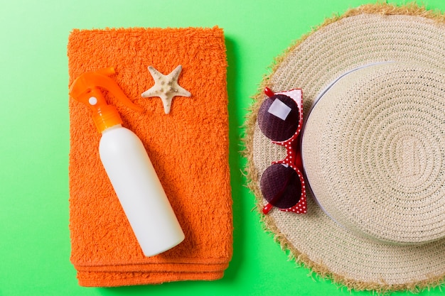 Accessoires de plage d'été à plat. Crème de bouteille de crème solaire, serviette et coquillages sur fond coloré. Concept de vacances de voyage avec espace de copie.