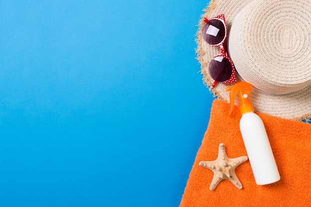 Accessoires de plage d'été à plat. Crème de bouteille de crème solaire, serviette et coquillages sur fond coloré. Concept de vacances de voyage avec espace de copie.