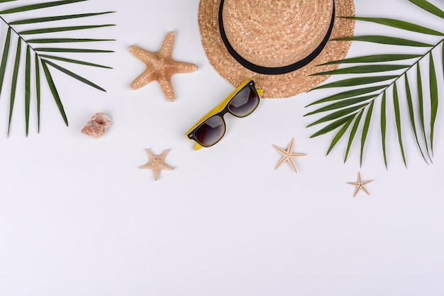 Accessoires de plage : lunettes et chapeau avec coquillages et étoiles de mer sur fond blanc. Fond d'été