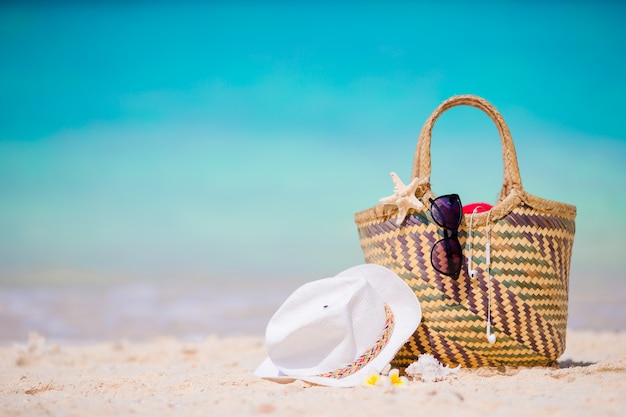 Photo accessoires de plage - sac de paille, chapeau blanc, étoile de mer et lunettes de soleil noires sur la plage. concept de plage d'été