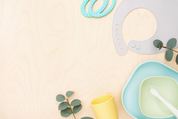 Accessoires pour bébé et vaisselle pour la nourriture sur fond en bois Premier concept d'alimentation pour les enfants Mise à plat Vue de dessus Espace pour le texte Tasse à bavoir en silicone sur fond neutre Servir de la nourriture pour bébé