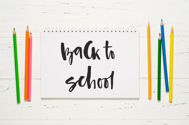 Accessoires pour enfants pour étudier la créativité et les fournitures de bureau sur un fond en bois blanc Inscription manuscrite Retour à l'école sur un cahier blanc