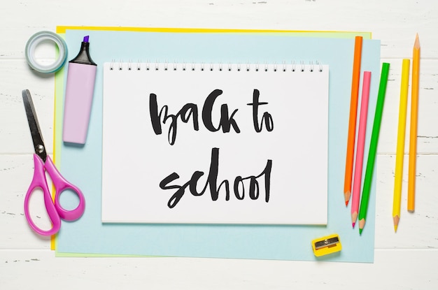 Accessoires pour enfants pour étudier la créativité et les fournitures de bureau sur un fond en bois blanc Inscription manuscrite Retour à l'école sur un cahier blanc