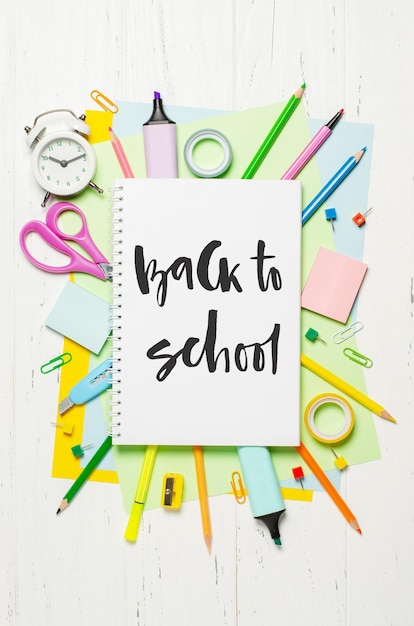 Accessoires pour enfants pour étudier la créativité et les fournitures de bureau sur un fond en bois blanc Inscription manuscrite Retour à l'école sur un cahier blanc