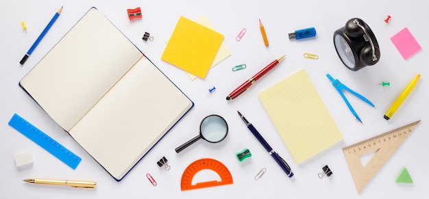 Accessoires scolaires et cahier ou livre ouvert avec des pages vides sur fond blanc, vue de dessus