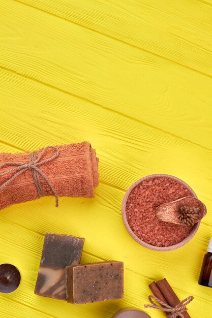 Accessoires de soins spa sur un bureau en bois jaune. Serviette roulée verticalement avec du sel et du savon.