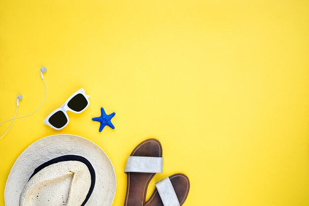 Accessoires de vacances d'été. Chapeau de paille, lunettes de soleil blanches, écouteurs et tongs sur fond jaune. Espace copie, mise à plat.