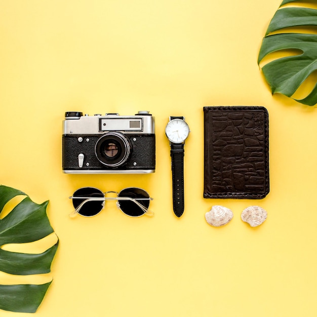 Accessoires de voyageur sur fond jaune avec appareil photo en feuille de palmier et lunettes de soleil à plat vue de dessus
