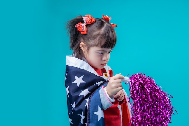 Accessoiriser extravagant. Fille curieuse aux cheveux noirs avec le syndrome de Down étant occupée avec la décoration du 4 juillet dans ses mains