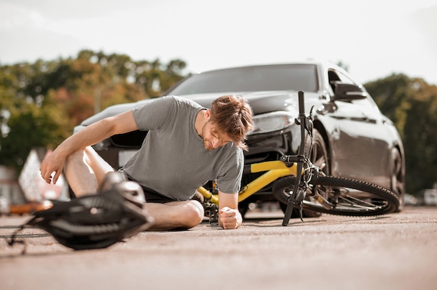 Accident sur la route. Dark haired bad feeling guy in sportswear tombant de vélo sur route devant une voiture noire