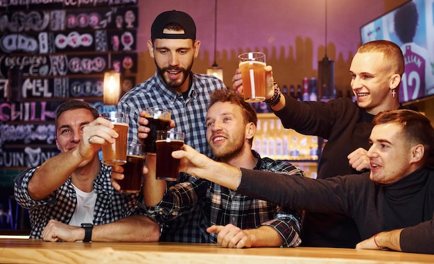 Acclamations en frappant des verres à bière Un groupe de personnes ensemble à l'intérieur du pub s'amuse le week-end