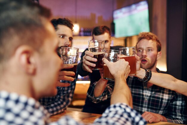 Acclamations en frappant des verres à bière Un groupe de personnes ensemble à l'intérieur du pub s'amuse le week-end