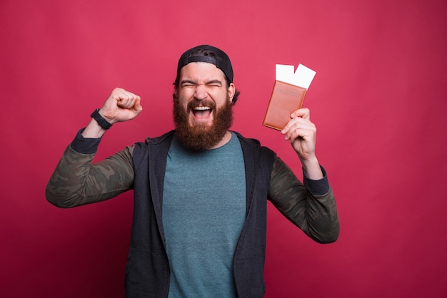 Acclamations de l'homme barbu tient un passeport avec des billets tout en faisant le geste du gagnant