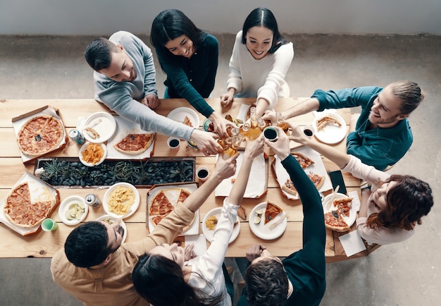 Acclamations! Vue de dessus de jeunes en tenue décontractée se grillant et souriant tout en dînant à l'intérieur