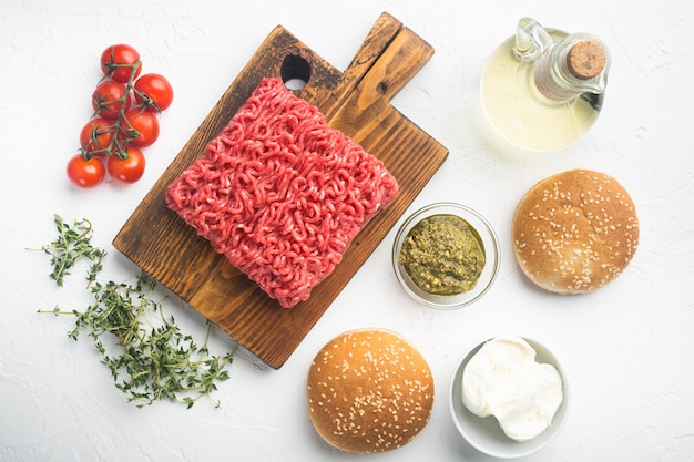 Accueil Ingrédients hamburgers de boulettes de viande de boeuf haché cru, sur une planche à découper en bois, sur une table en pierre blanche, vue de dessus à plat