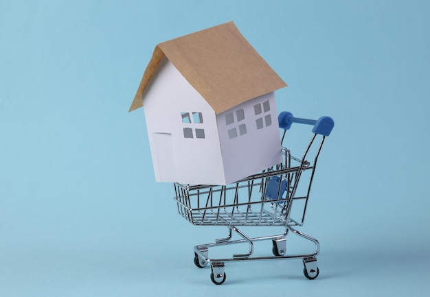 Achat maison Mini figurine de maison en papier dans un chariot de supermarché sur fond bleu