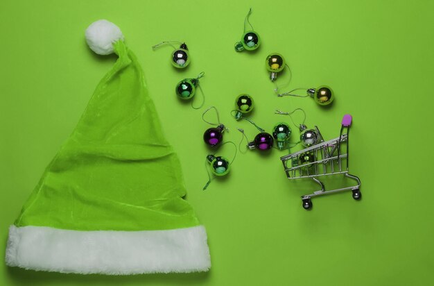 Achat de noël. Bonnet de Noel, panier, boules de noël sur fond vert. Vue de dessus