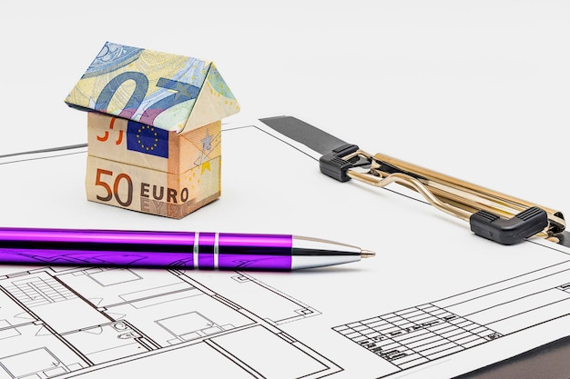 Achat et vente de logement Hypothèque pour l'achat d'une maison Propriété locative Maison faite de billets en euros et d'un stylo à bille sur le projet de la future maison Espace de copie en gros plan