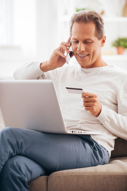 Achats directement de chez vous. Cheerful man shopping en ligne alors qu'il était assis sur le canapé à la maison