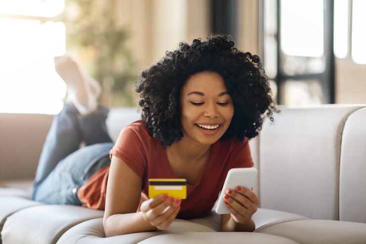 Photo achats en ligne femme noire souriante à l'aide d'un smartphone et d'une carte de crédit à la maison
