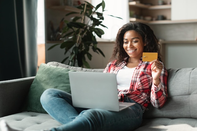 Photo achats en ligne grande vente une dame noire du millénaire souriante utilise un ordinateur et une carte de crédit pour vérifier son compte