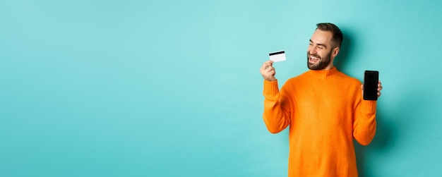 Photo achats en ligne homme satisfait utilisant une carte de crédit et montrant l'écran du mobile personne satisfaite