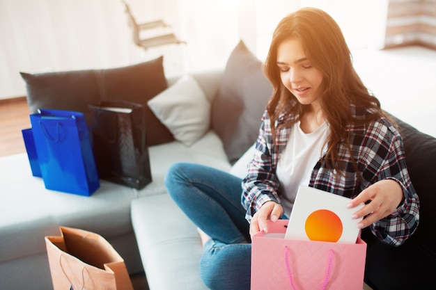 Achats en ligne, une jeune femme a commandé une livraison à domicile. Maintenant, elle s'assoit sur le canapé et déballe ses nouveaux achats.