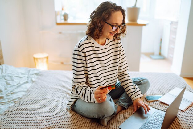 Achats en ligne à la maison Une jeune femme détient une carte de crédit et utilise un ordinateur portable Vente du vendredi noir