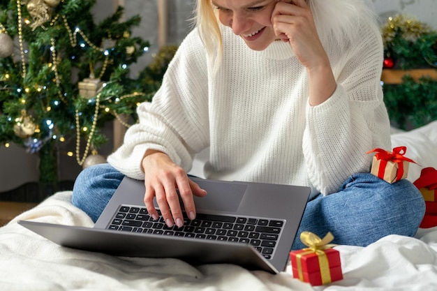 Achats en ligne de Noël Une acheteuse passe une commande sur un ordinateur portable Une femme achète des cadeaux pour se préparer à Noël parmi les coffrets cadeaux et les forfaits