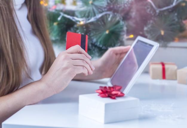 Achats en ligne de Noël. Femme floue en pull blanc achète des cadeaux de Noël avec ordinateur portable et tenant une carte de crédit