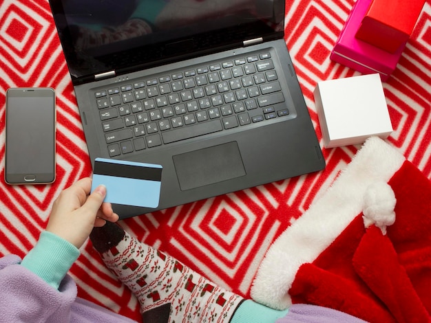 Achats en ligne de Noël. fille en pyjama et chaussettes avec un imprimé de Noël commande des cadeaux sur Internet à l'aide d'un ordinateur portable. une fille commande des cadeaux sur Internet à l'aide d'un ordinateur portable.