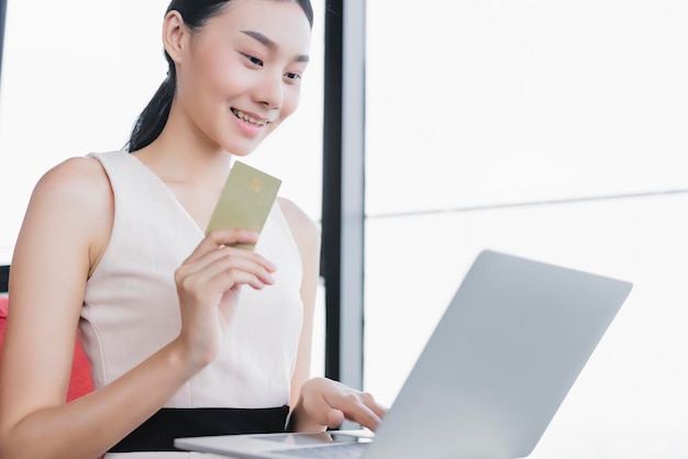 Achats en ligne réussis avec une belle femme asiatique main présente un ordinateur portable et une carte de crédit avec bonheur souriant