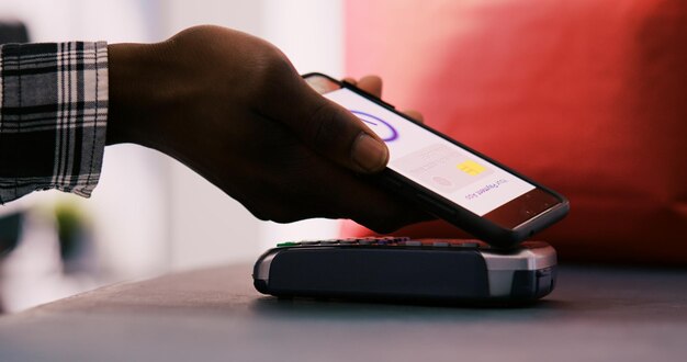 Photo un acheteur afro-américain met son téléphone sur un terminal de point de vente après avoir acheté des marchandises et des accessoires élégants dans un magasin de vêtements. client payant pour des vêtements décontractés à la mode au comptoir. fermer.