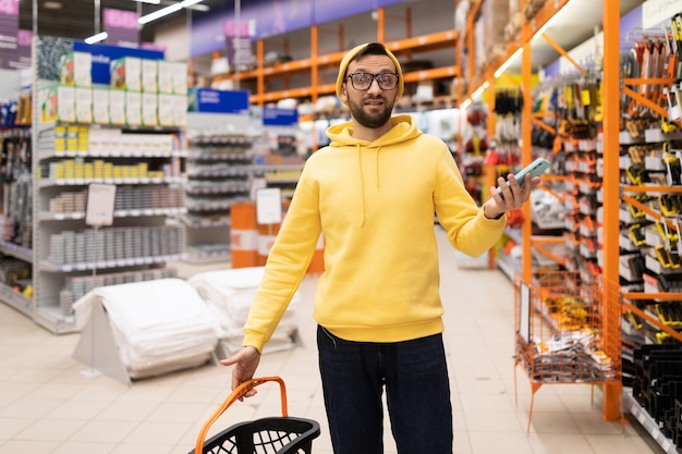 Un acheteur confus dans un hypermarché de construction agitant ses mains de surprise dans la perplexité