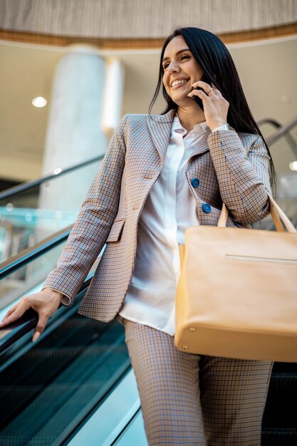 Acheteur de femme d'affaires souriante posant à l'escalator et smartphone parlant