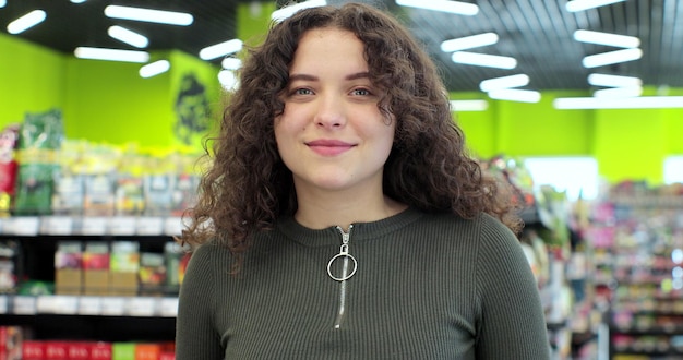 Acheteur femme stand étagère supermarché intérieur Portrait jeune femme se tient devant la caméra dans un supermarché