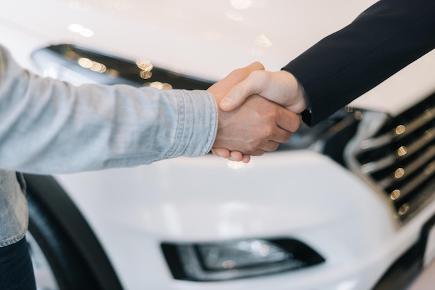 Acheteur de voiture serrant la main du vendeur dans un concessionnaire automobile, devant la voiture. Gros plan sur une poignée de main de gens d'affaires méconnaissables. Concept de choix et d'achat d'une nouvelle voiture dans la salle d'exposition.