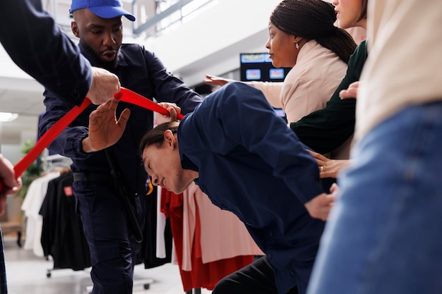 Photo des acheteurs fous se précipitent dans un centre commercial local pour obtenir les meilleures offres du black friday, un agent de sécurité afro-américain retenant une foule de personnes diverses et enthousiastes à l'entrée du magasin de vêtements