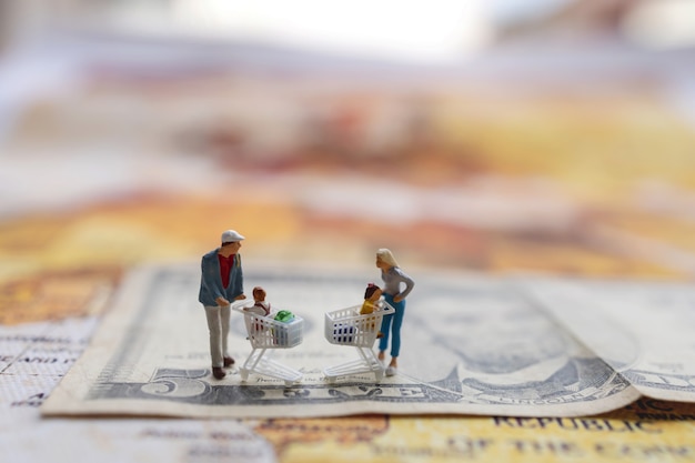 Acheteurs miniatures avec panier debout sur la carte de l'argent et du monde.