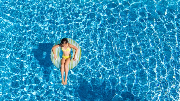 Acrive fille dans la piscine vue aérienne de dessus, enfant nage sur l'anneau gonflable beignet, l'enfant s'amuse dans l'eau bleue sur la station de vacances en famille