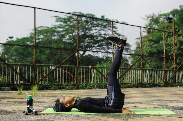 Acrive jeune homme faisant des levées de jambe au tapis de yoga en plein air