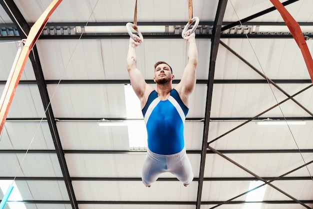 Acrobate d'homme et gymnastique se balançant sur des anneaux en forme pour s'entraîner ou s'entraîner au gymnase