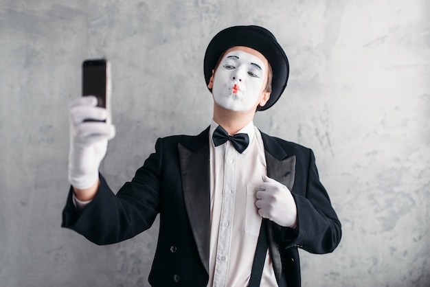 Acteur de pantomime avec masque de maquillage fait selfie devant la caméra. Comédien en costume, gants et chapeau