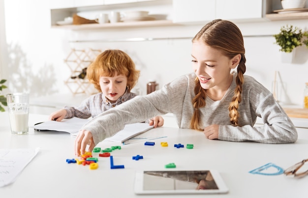 Activité créative. Lumineuse jolie fille enthousiaste enseignant à son frère le calcul à l'aide d'une forme de jeu spéciale tout en passant la matinée ensemble à la maison