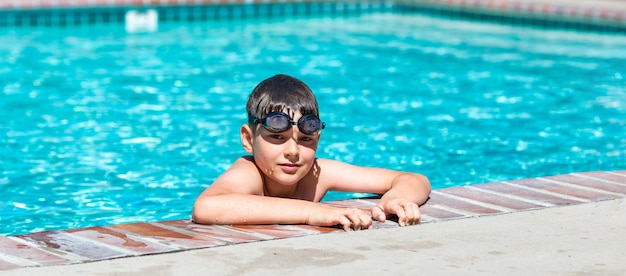 Photo activité estivale extérieure concept de santé et de vacances amusantes un garçon heureux de huit ans portant des lunettes de natation se tient au bord de la piscine par une chaude journée d'été