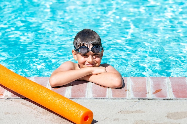 Photo activité estivale extérieure concept de santé et de vacances amusantes un garçon heureux de huit ans portant des lunettes de natation se tient au bord de la piscine par une chaude journée d'été