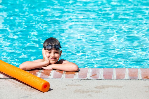 Photo activité estivale extérieure concept de santé et de vacances amusantes un garçon heureux de huit ans portant des lunettes de natation se tient au bord de la piscine par une chaude journée d'été