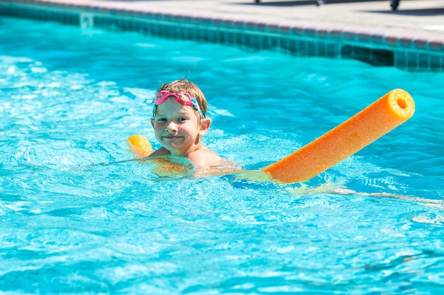 Photo activité estivale en plein air concept de santé et de vacances amusantes heureux garçon souriant de cinq ans dans des lunettes de natation nager dans la piscine avec des nouilles dans une chaude journée d'été