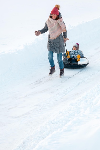 Activité hivernale de la mère et de l'enfant de la famille ensemble sur des tubes à neige sur la route des neiges d'hiver